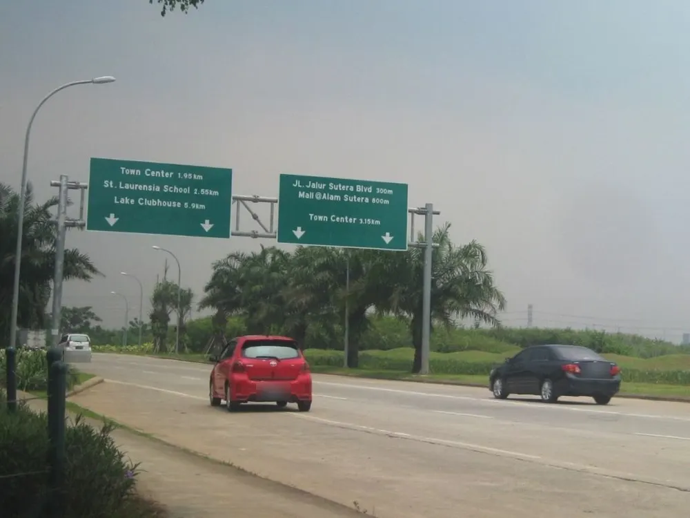 Jalan utama Alam Sutera di Tangerang Selatan dengan rambu penunjuk arah hijau, sebuah mobil merah, dan sebuah sedan hitam
