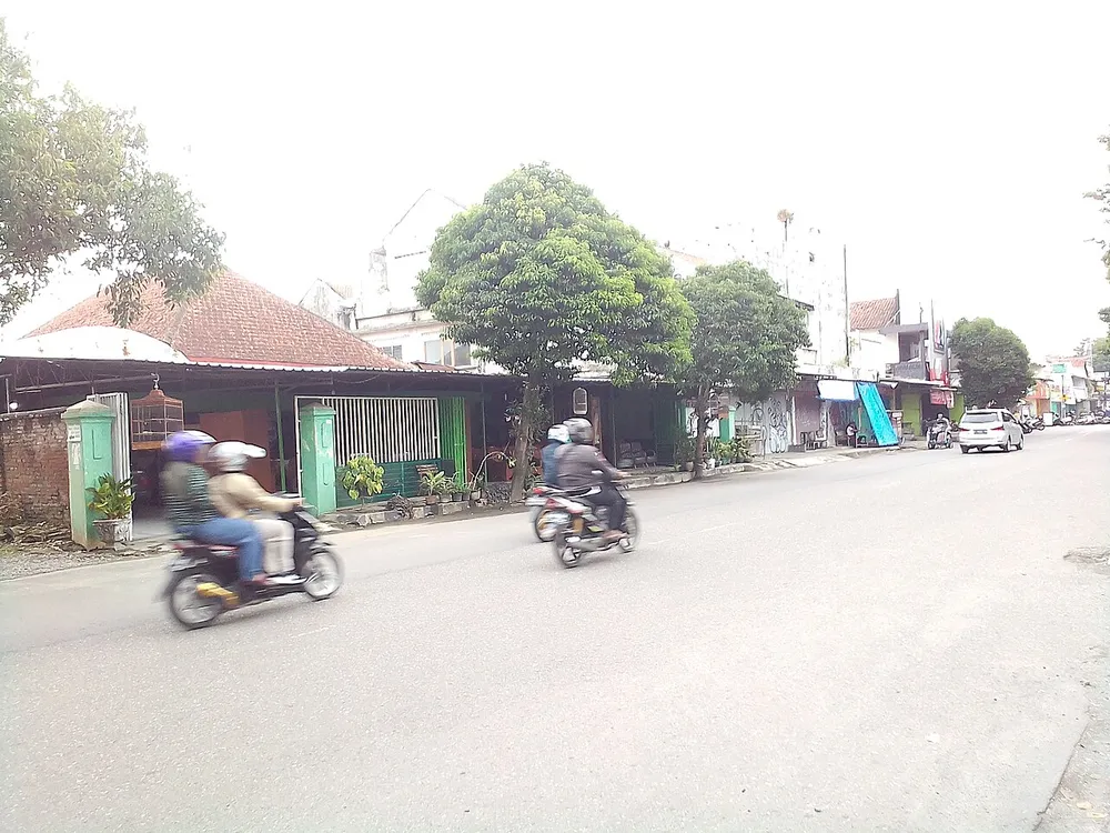 Dua sepeda motor skuter melintas di Jalan Pemuda, Kebumen, dengan deretan rumah dan pepohonan di tepi jalan