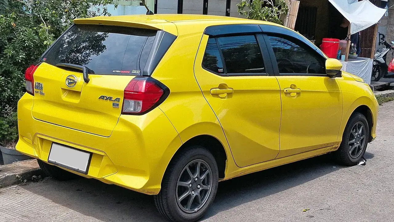 Bagian belakang Daihatsu Ayla 1.2 R generasi kedua berwarna kuning di tepi jalan, terlihat spoiler belakang, wiper belakang, emblem Ayla, dan velg alloy
