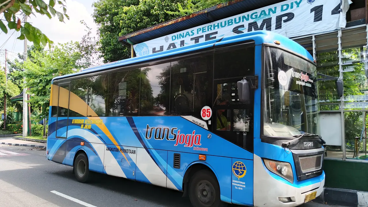 Bus sedang Isuzu Elf NQR 71 berkaroseri Laksana dengan livery biru putih Trans Jogja, berhenti di depan halte SMP