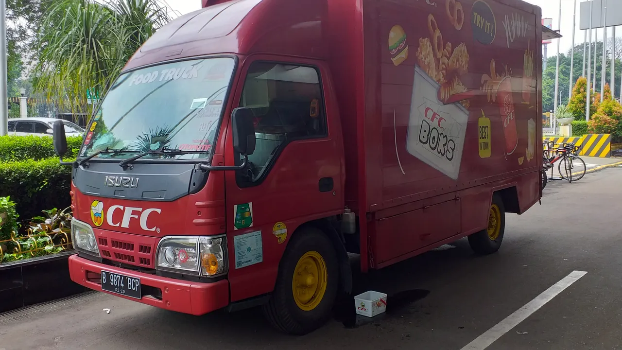 Truk Isuzu Elf berkabin merah dengan boks karoseri bergambar menu makanan, difungsikan sebagai food truck dan terparkir di tepi jalan