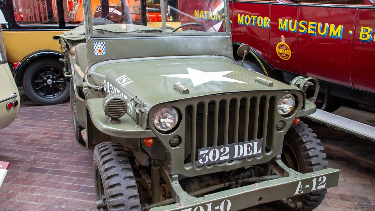 Willys MB berwarna hijau zaitun dengan bintang putih di kap mesin, gril tujuh bilah vertikal, dan pelat 302 DEL, dipajang di museum