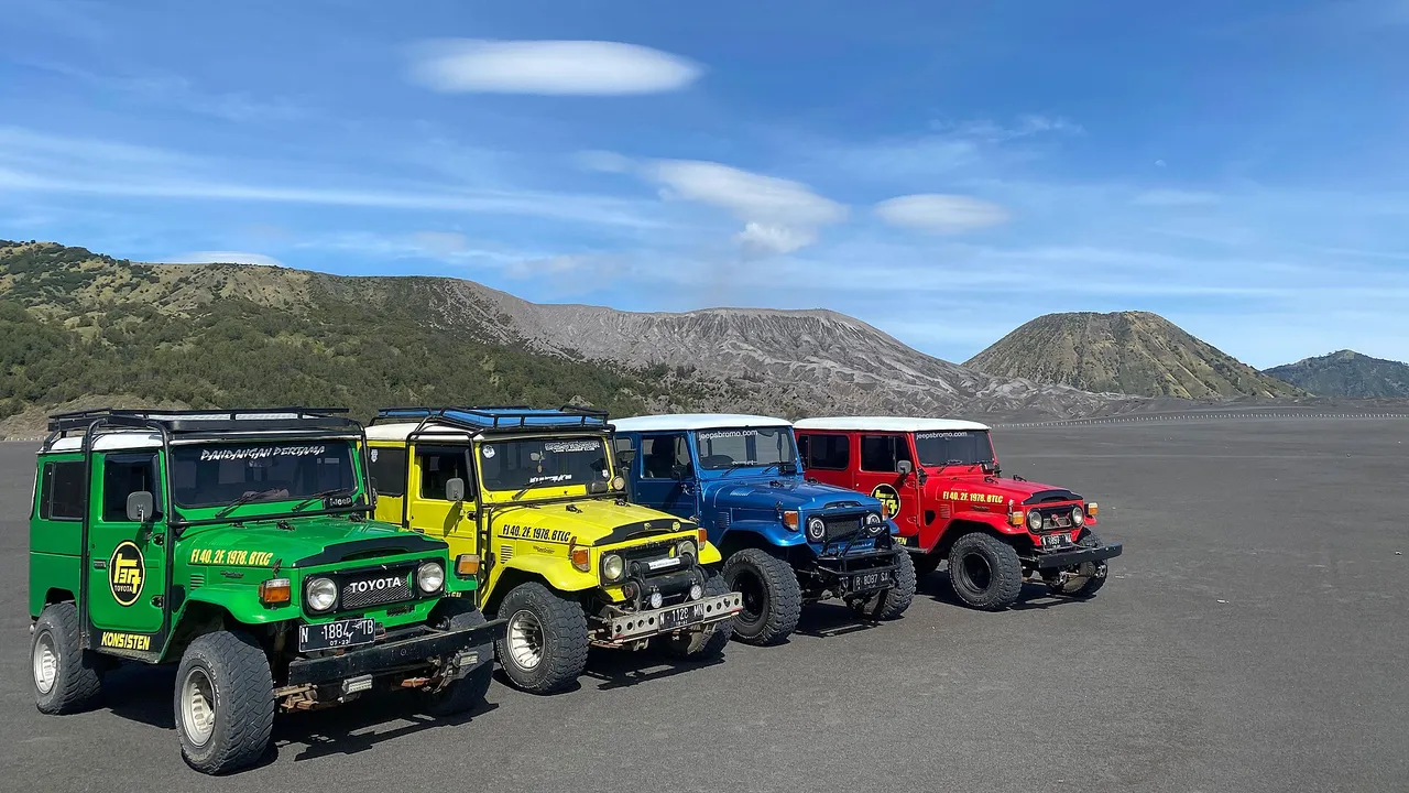 Empat Toyota Land Cruiser FJ40 berwarna hijau, kuning, biru, dan merah berjajar di lautan pasir Bromo dengan bukit di latar belakang