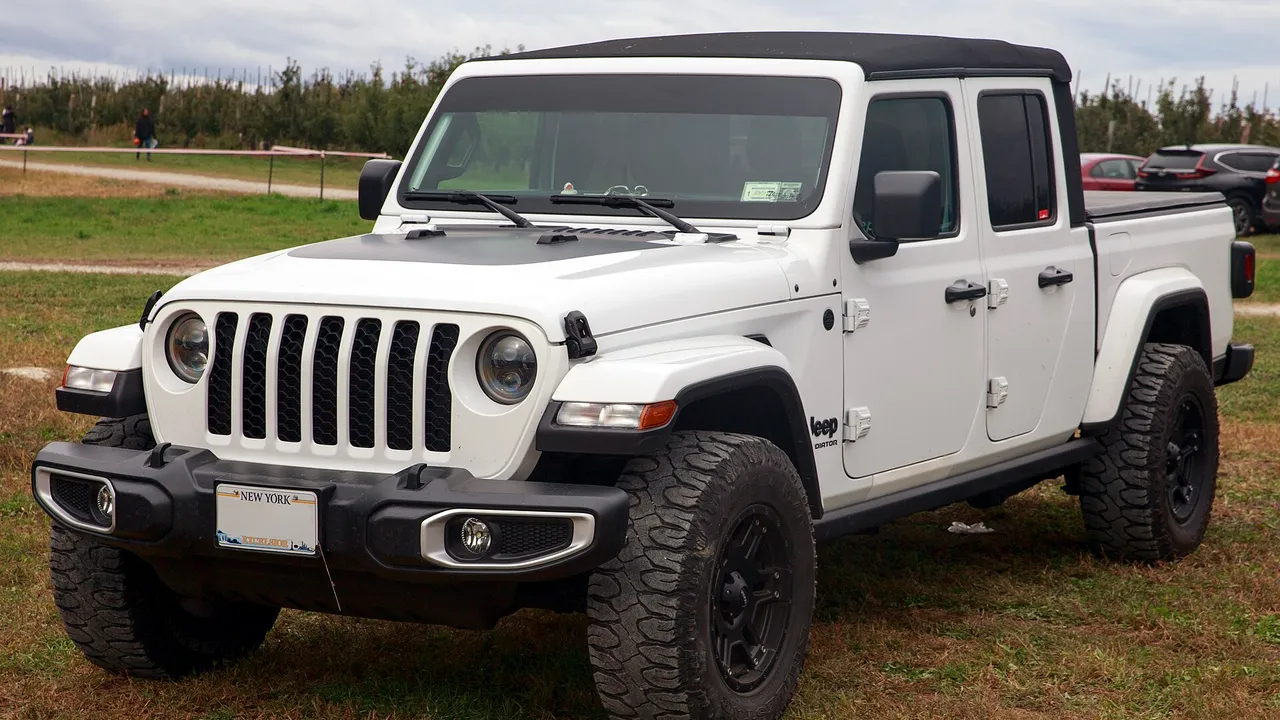 Jeep Gladiator Sport berwarna putih dengan atap hitam, gril tujuh bilah, dan ban all-terrain terparkir di lapangan rumput