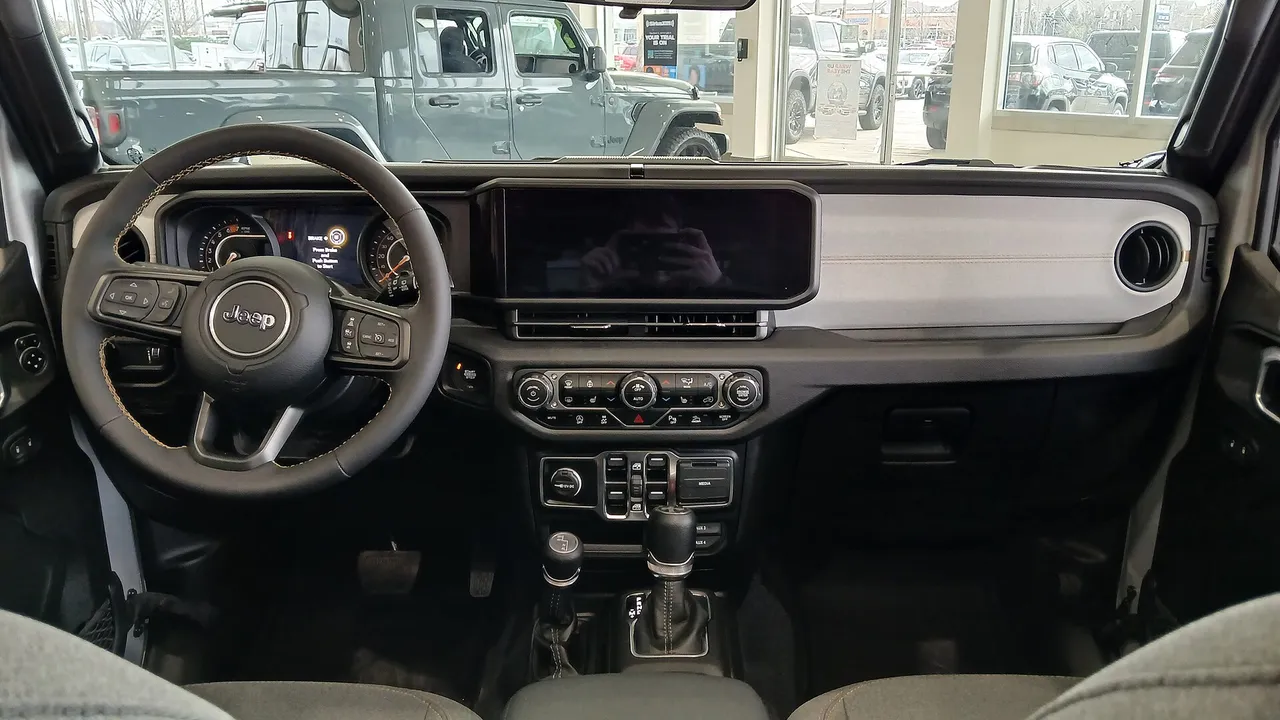Dasbor Jeep Wrangler Unlimited 2024 dengan layar sentuh lebar di tengah, setir berlogo Jeep, tuas transmisi otomatis, dan tuas transfer case