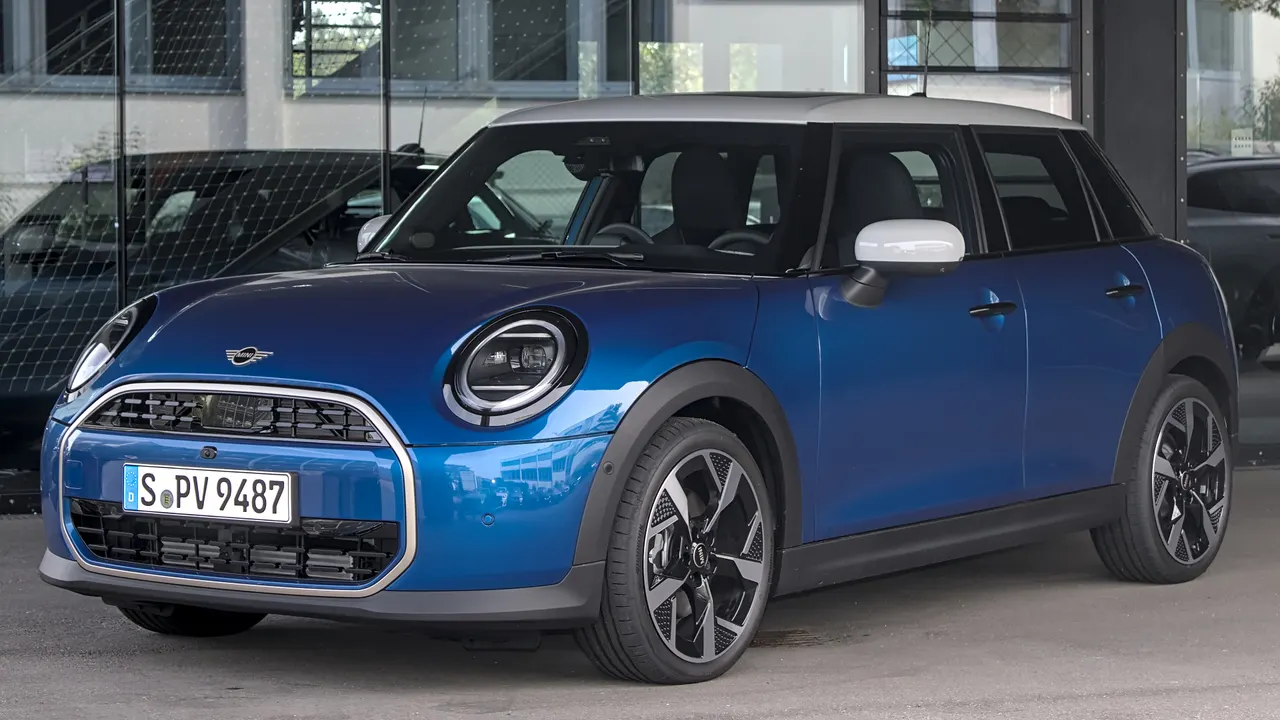 MINI Cooper lima pintu generasi F65 berwarna biru dengan atap abu-abu muda, lampu bulat, dan gril segi delapan, terparkir di depan gedung