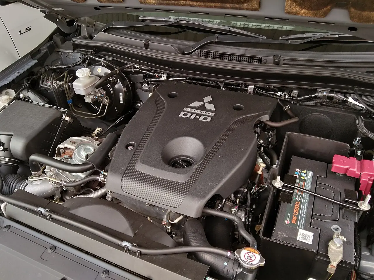 Ruang mesin dengan penutup mesin hitam bertuliskan Common Rail DI-D dan logo Mitsubishi, turbo terlihat di sisi kiri