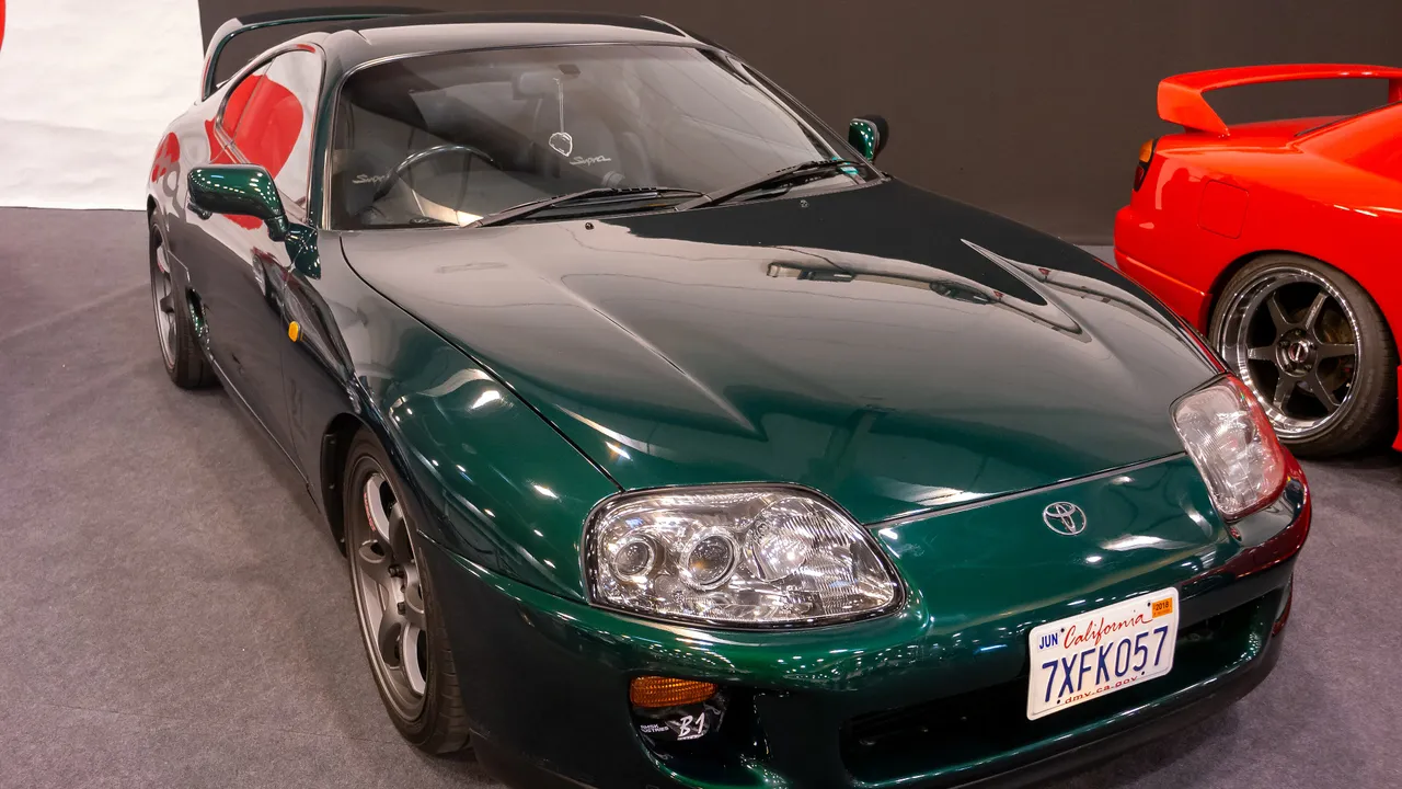 Toyota Supra generasi keempat A80 berwarna hijau tua dengan lampu proyektor bulat dan pelat California, dipajang di pameran otomotif