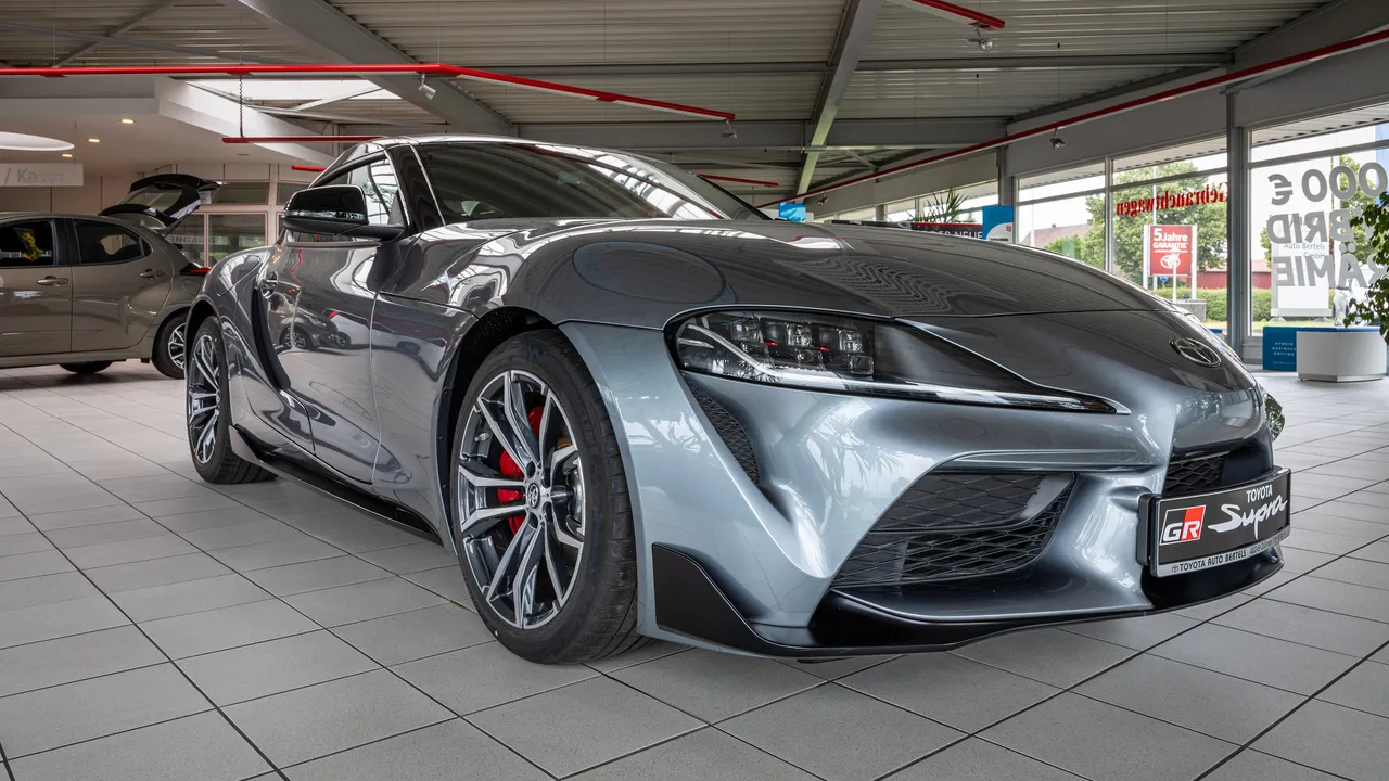 Toyota GR Supra generasi kelima berwarna abu-abu metalik di ruang pamer dealer, terlihat kaliper rem merah dan pelat bertulisan GR Supra