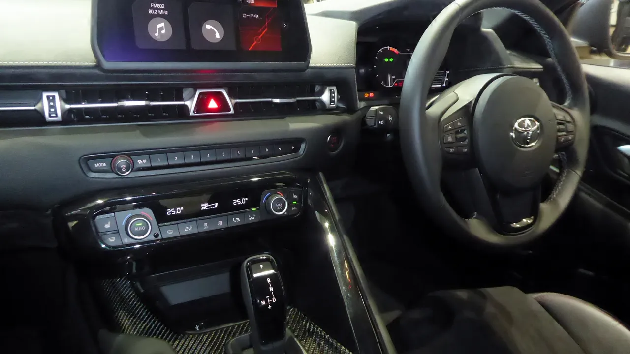 Interior Toyota GR Supra setir kanan dengan layar tengah, tombol pengatur AC, tuas transmisi otomatis, dan setir berlogo Toyota