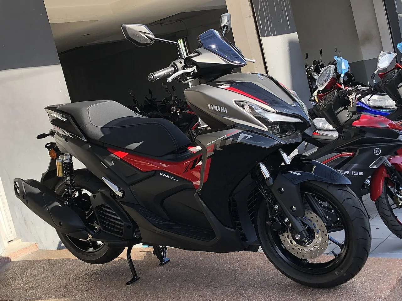 Yamaha Aerox 155 ABS model 2025 abu-abu dan merah dengan bodi generasi baru, terparkir di depan deretan sepeda motor