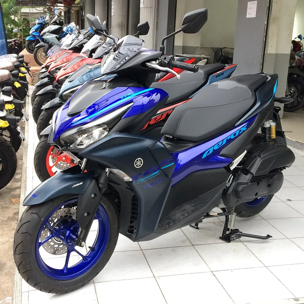 Yamaha Aerox 155 biru dengan logo ABS di spakbor depan berjajar dengan skuter lain yang dipajang