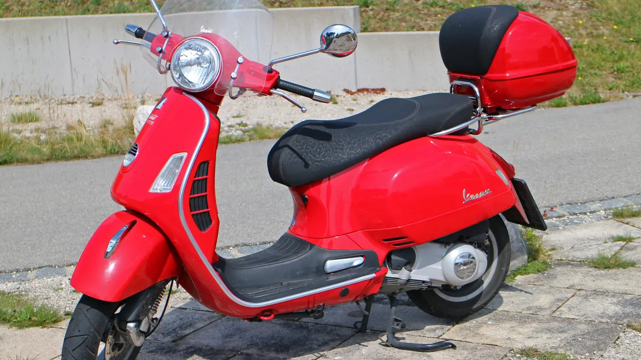Vespa GTS 250ie merah dengan jok hitam, kotak bagasi merah, dan velg alloy, diparkir di tepi jalan