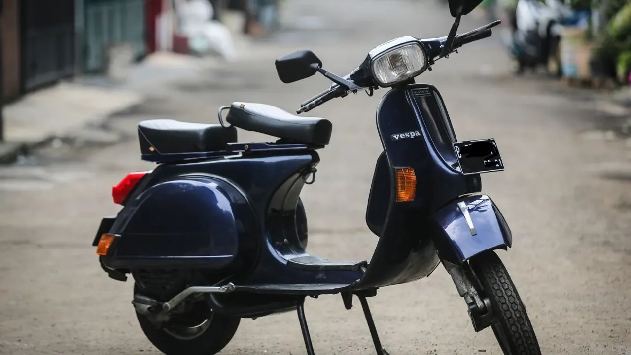 Vespa P150XE Exclusive 2 berwarna biru tua dengan jok ganda hitam dan lampu depan persegi, terparkir di gang