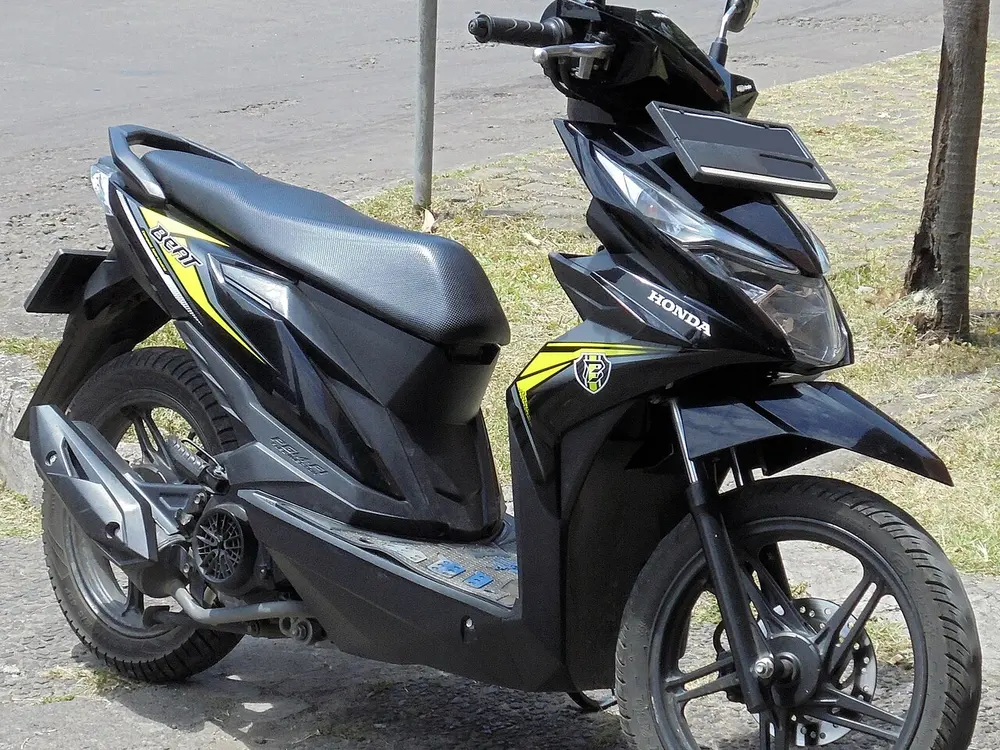 Honda BeAT eSP CBS 110 warna hitam bergaris kuning terparkir di pinggir jalan, sisi kiri memperlihatkan penutup CVT dan roda belakang
