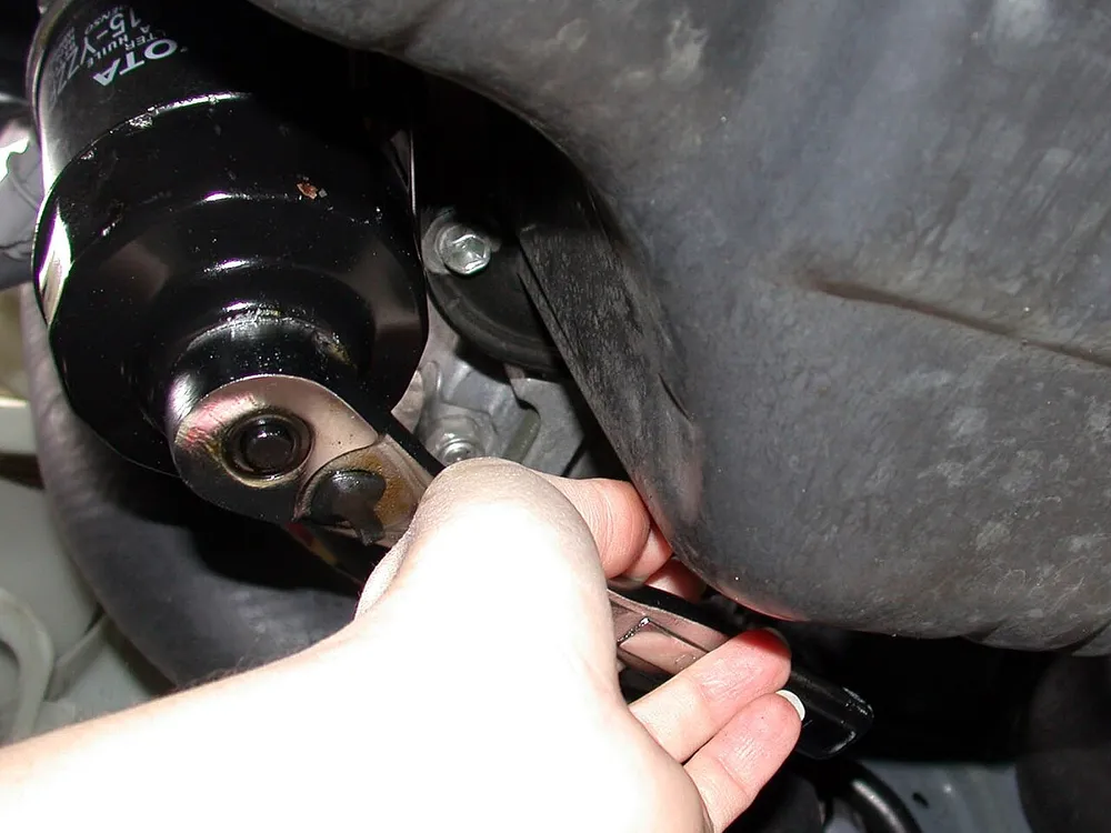 Kunci filter oli dipasang pada tabung filter oli hitam di kolong mobil
